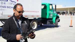 Commercial driving instructor reviewing tablet in front of truck.