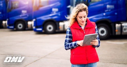 Woman standing in front of commercial trucks looking down at notepad.